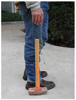 A construction worker stands next to a sledge hammer to demonstrate the proper handle length