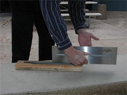 Trowel maintenance showing a board on the floor with a worker moving the trowel over it