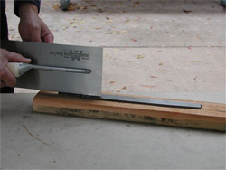 A worker shows how to move the trowel across a board to keep it sharp.