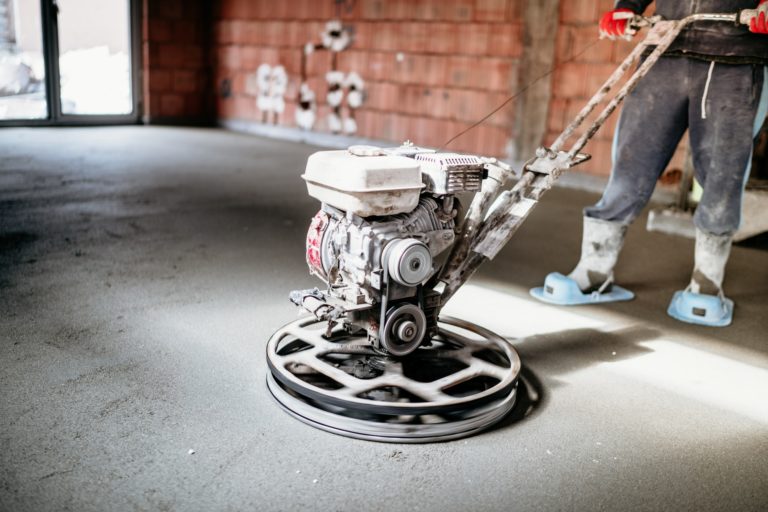 Worker with power trowel tool finishing concrete floor, screed, smooth concrete surface