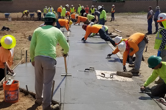 A group of cement masons learning how to construct a sidewalk as they are paid to learn